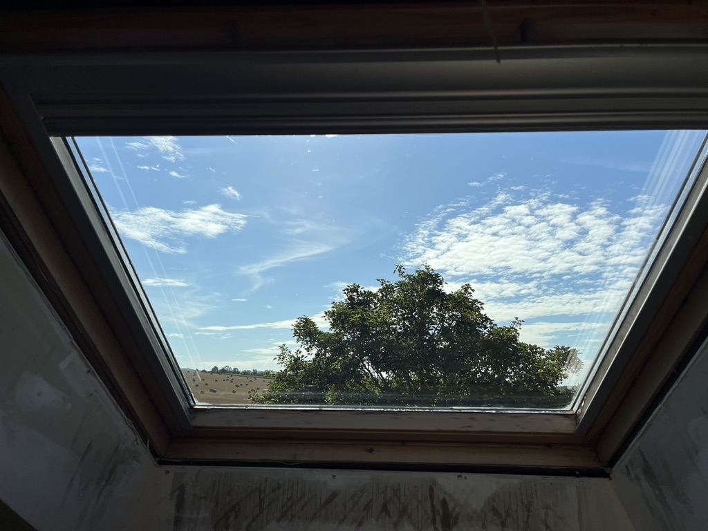Fenêtre de toit après nettoyage, avec une vue dégagée sur le ciel et les arbres.