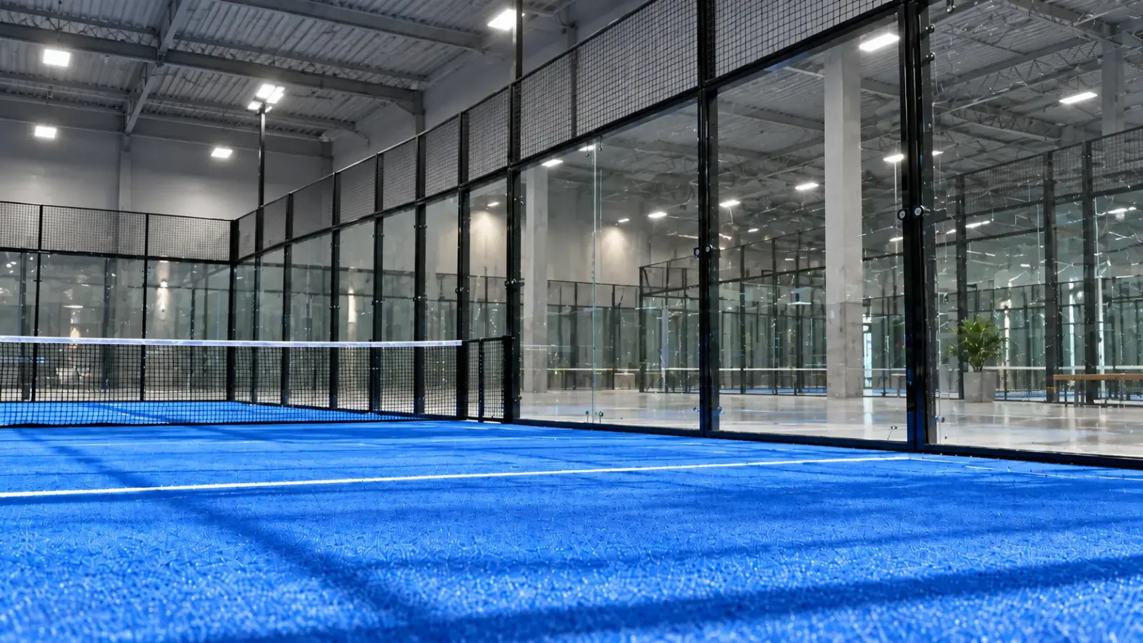 Terrain de padel couvert avec parois vitrées et gazon synthétique bleu