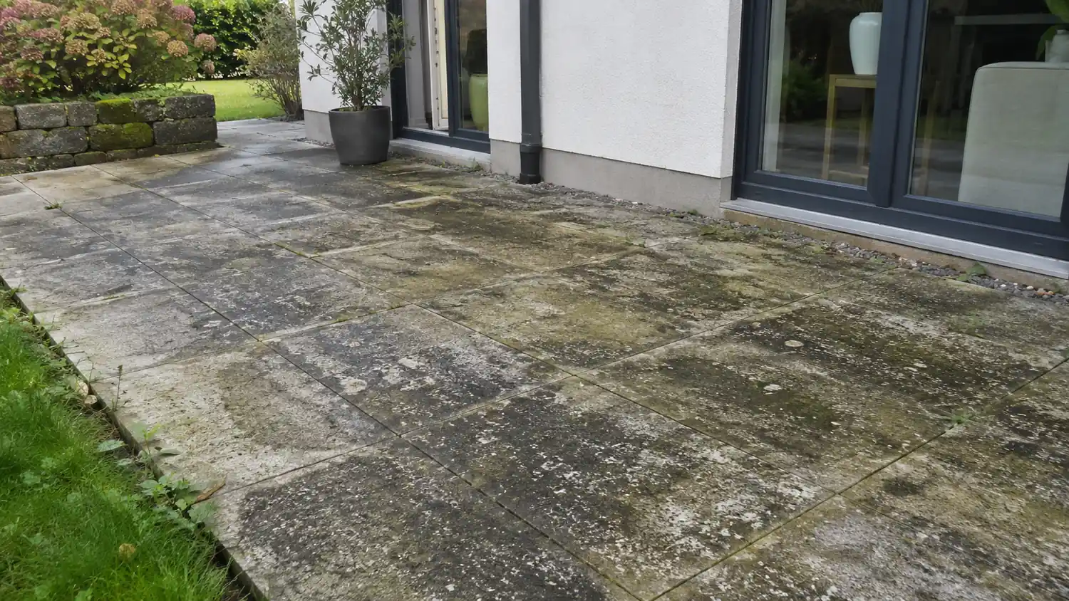 Terrasse en dalles avec mousses et traces vertes avant nettoyage, devant une baie vitrée