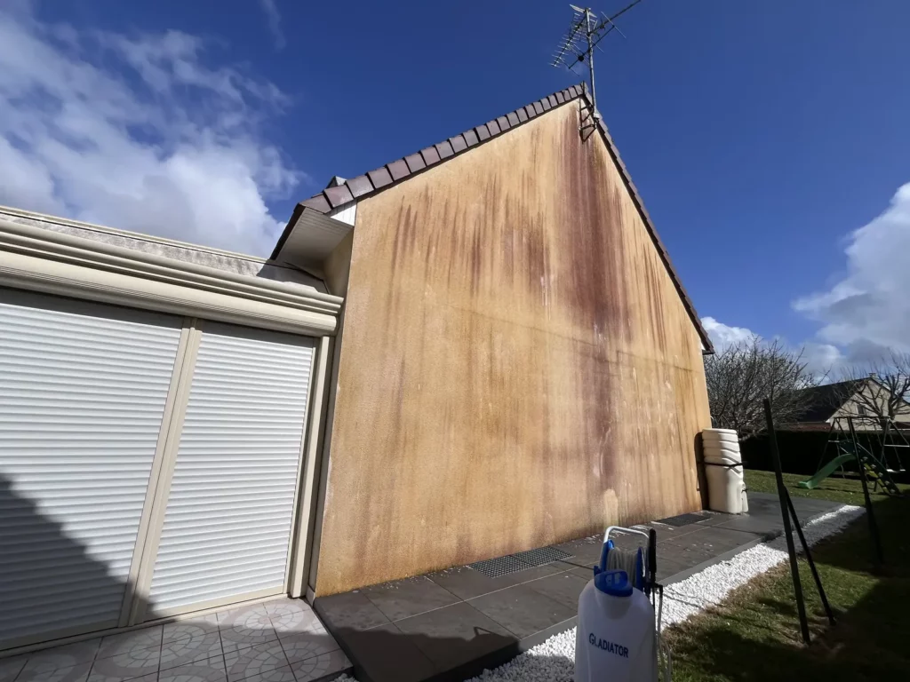 Façade avant nettoyage : larges coulures orangées sur l'enduit du pignon